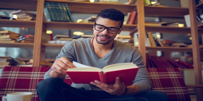 Smiling African American student enjoying book reading in library